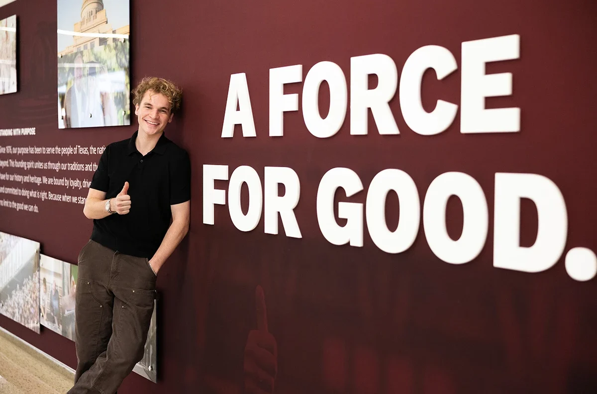 Portrait of Aiden Ross next to Texas A&M "a force for good" wall artwork