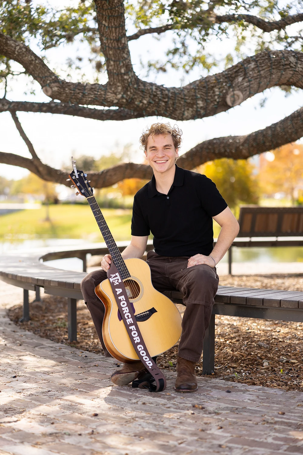 Portrait of Aiden Ross holding his acoustic guitar in Aggie Park