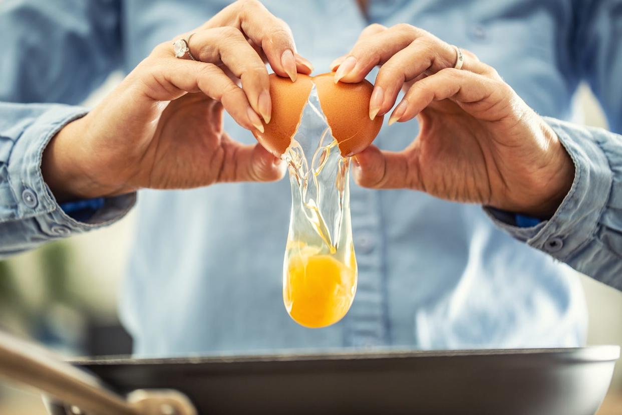 benefits of choline a detail of cracked egg falling into the pan as woman holds egg shells in both hands.