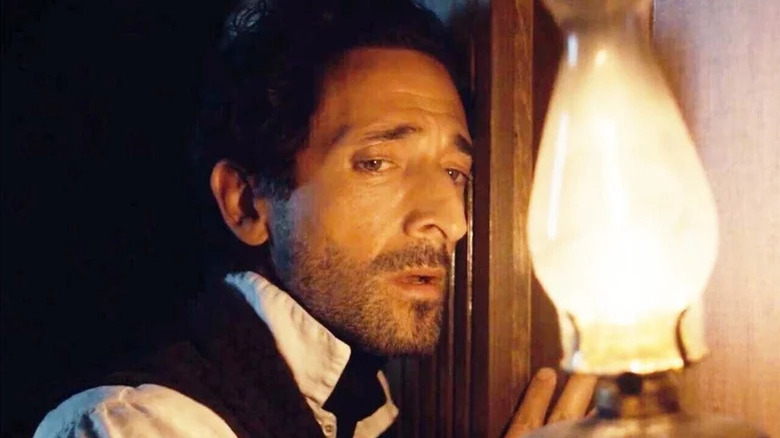 Charles Boone (Adrien Brody) listens against a wall while holding a gaslamp in Chapelwaite
