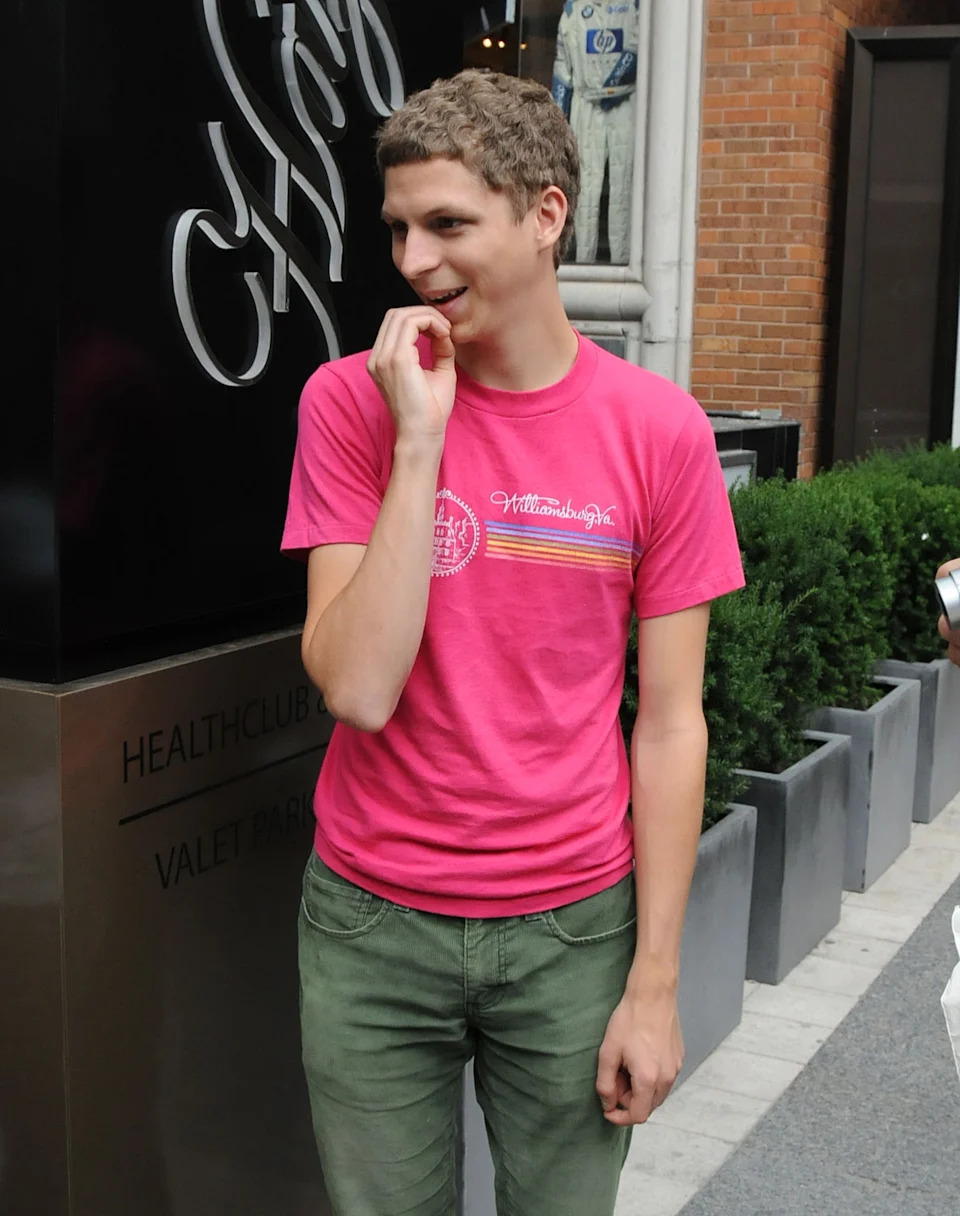 Person standing outdoors, smiling, wearing a casual T-shirt and pants