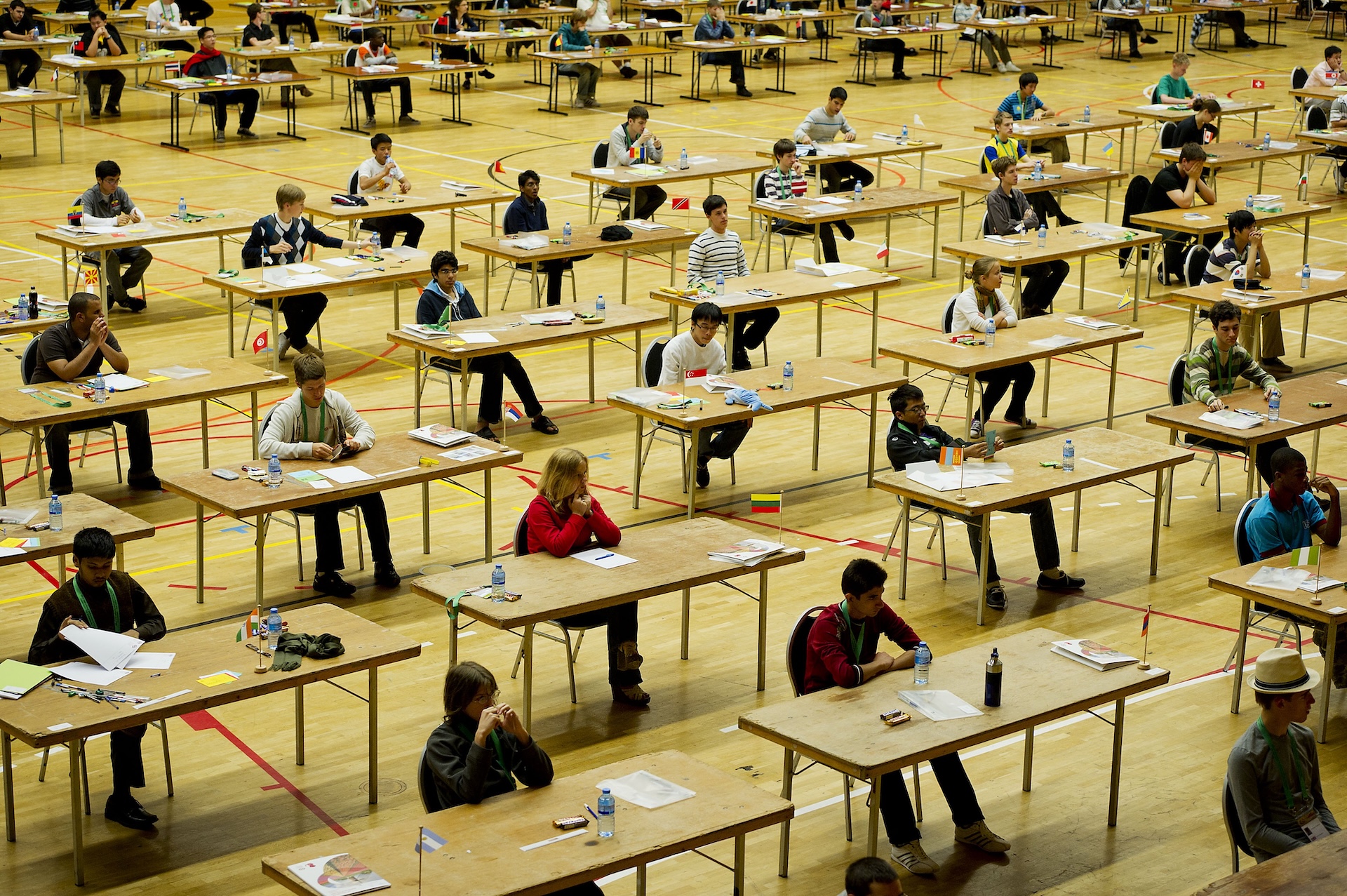 dozens of students sit in a hall working at desks