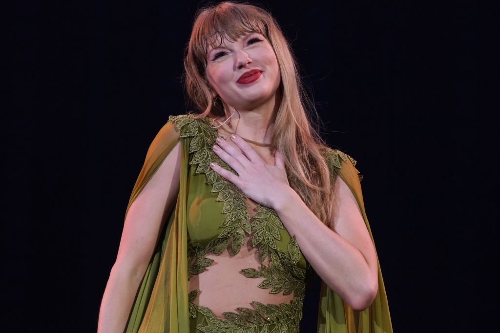 Taylor Swift performing live in a green gown with intricate leaf designs.