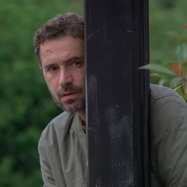 emmerdale john sugden outside hiding behind a wooden post