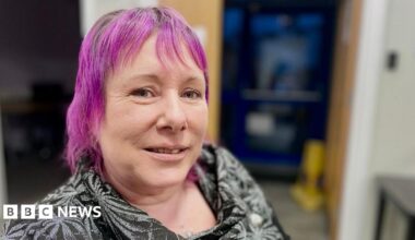 Leanne Nagel poses close to the camera. She has dyed purple hair and is wearing a black patterned blouse.