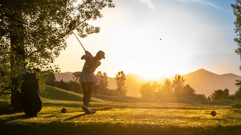 Golfer in mid-swing at sunset on course