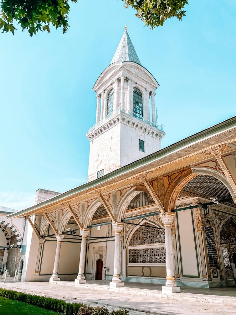 A white tower with a pointed roof overlooks an ornate Turkish palace