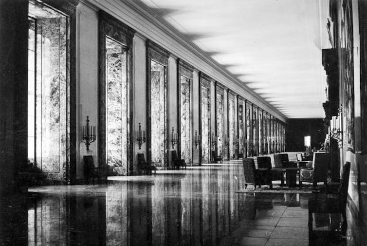 A black and white image of a large long hall made of reflective marble