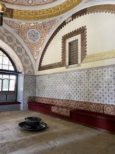 An intricately tiled room in a Turkish palace with a small window covered with a gold grill.