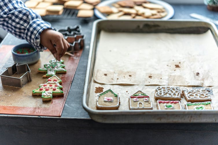 A child's hand putting sprinkles on a cookie and a cookie sheet with decorated cookies on it