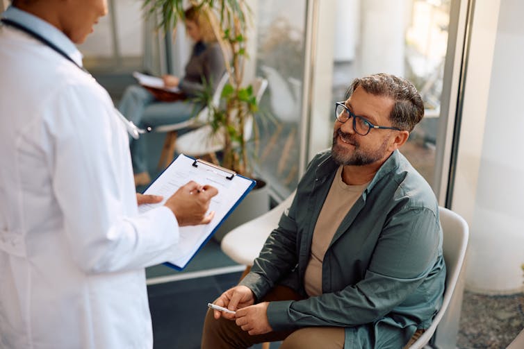 Seated man talks to a doctor in a clinic waiting room.