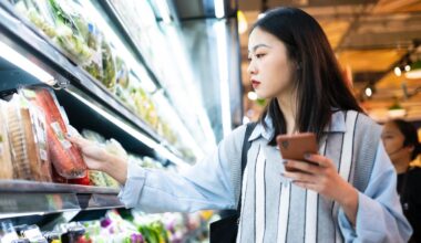A photo of a woman in a grocery store, looking at foods and her phone