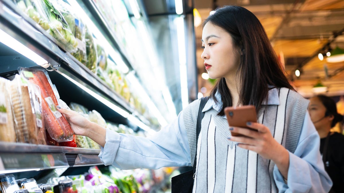 A photo of a woman in a grocery store, looking at foods and her phone