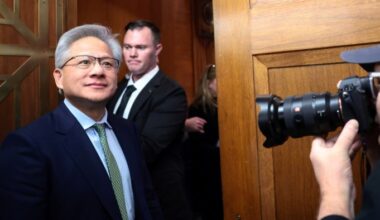 Jensen Huang stands in a hallway, looking ahead, as a photographer takes his picture.