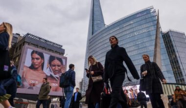 Commuters walk across London Bridge past a large ASOS advertisement, with The Shard and a modern glass office building in the background.