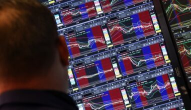 A trader looks at multiple monitors displaying stock charts and market data at the New York Stock Exchange.