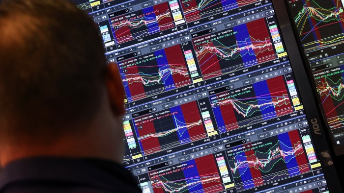 A trader looks at multiple monitors displaying stock charts and market data at the New York Stock Exchange.