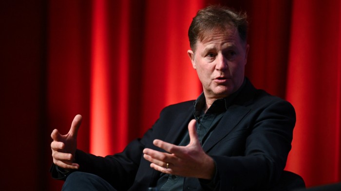 Nick Clegg gestures while speaking on stage against a red curtain backdrop.