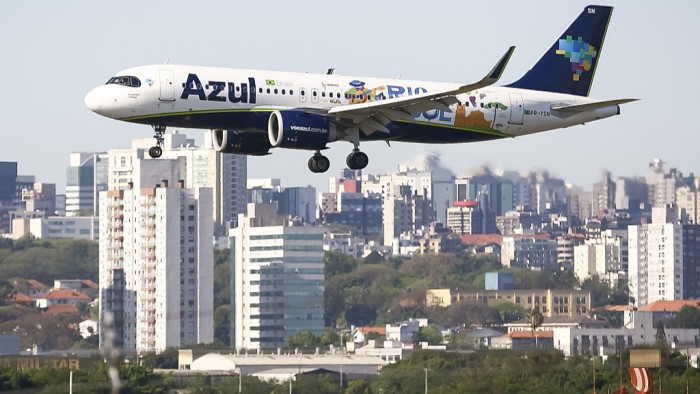 Azul Airbus A320 lands at Salgado Filho airport with city buildings in the background, marking the airport’s reopening after flood repairs.