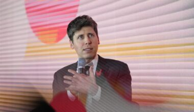 Sam Altman speaks into a microphone while gesturing with his hand at the AI Action Summit in Paris.