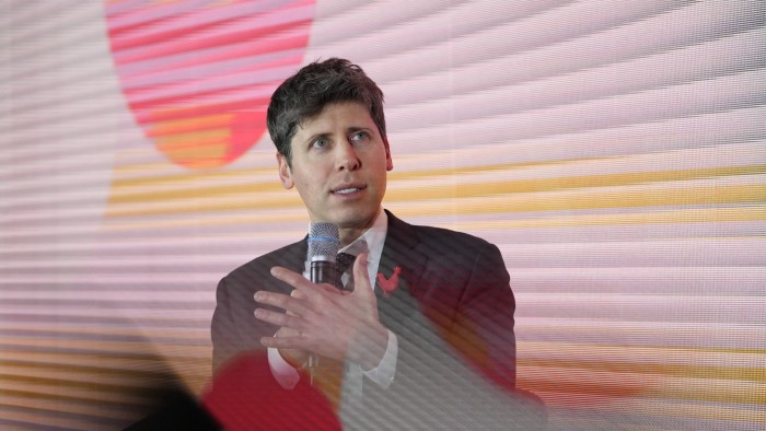 Sam Altman speaks into a microphone while gesturing with his hand at the AI Action Summit in Paris.