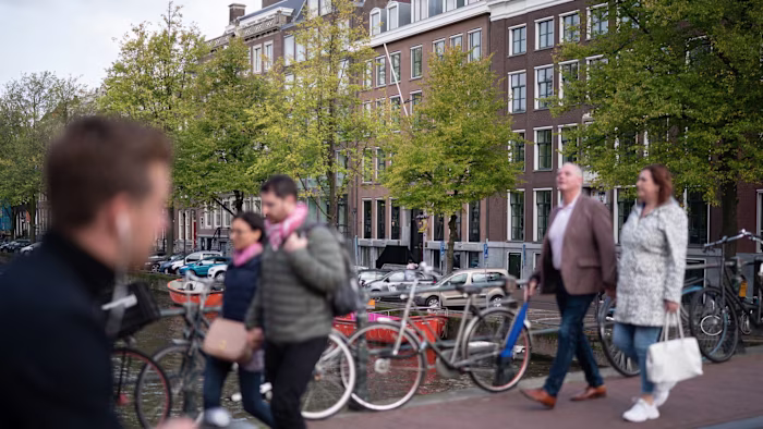 People walk across a bridge over the Keizersgracht canal in Amsterdam with bicycles parked nearby.