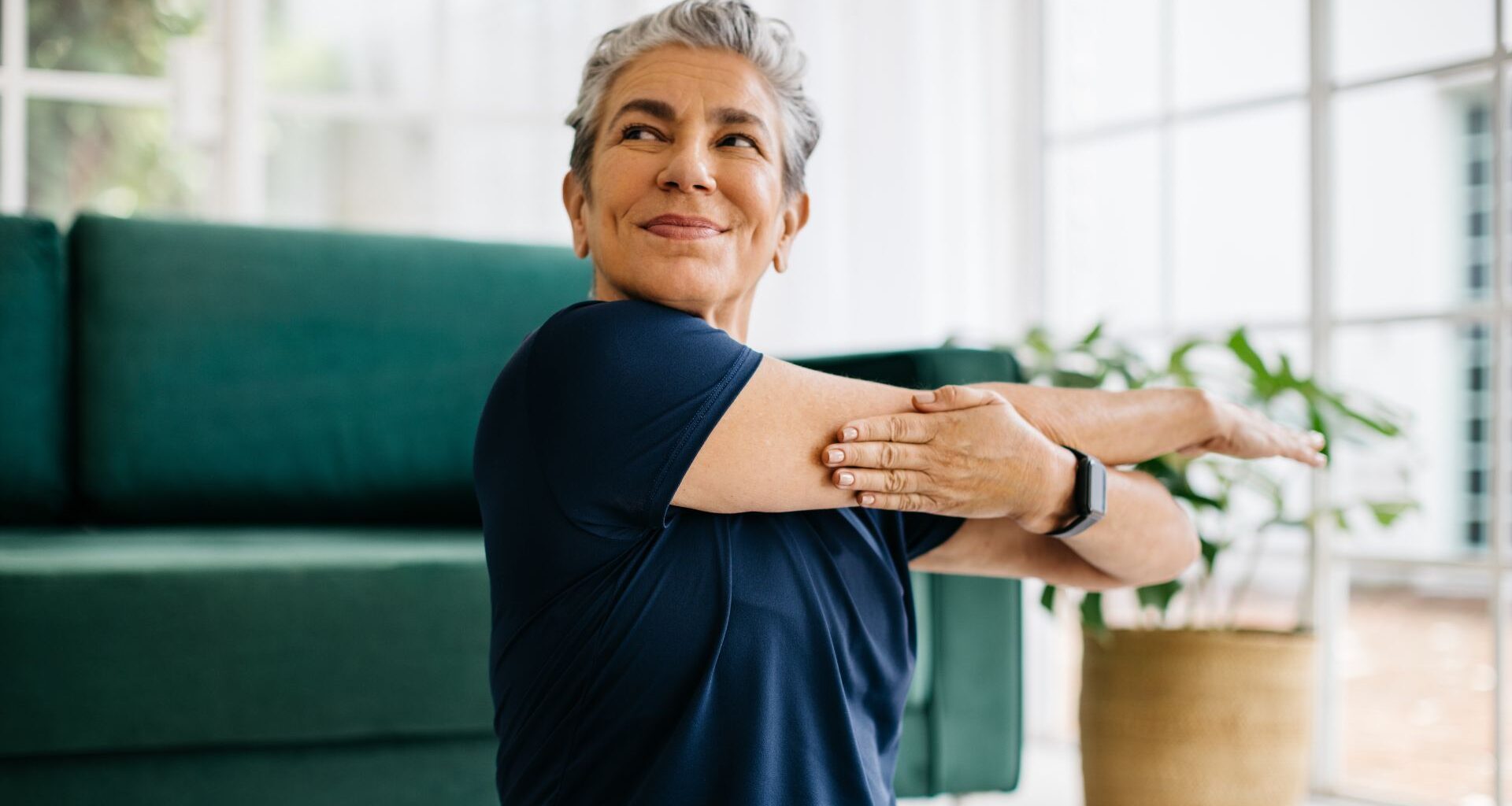 Woman doing yoga for strength work, sitting on living room floor and stretching