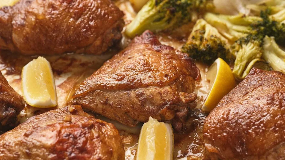 One pan chicken thighs with crispy skin, served with lemon wedges and broccoli.