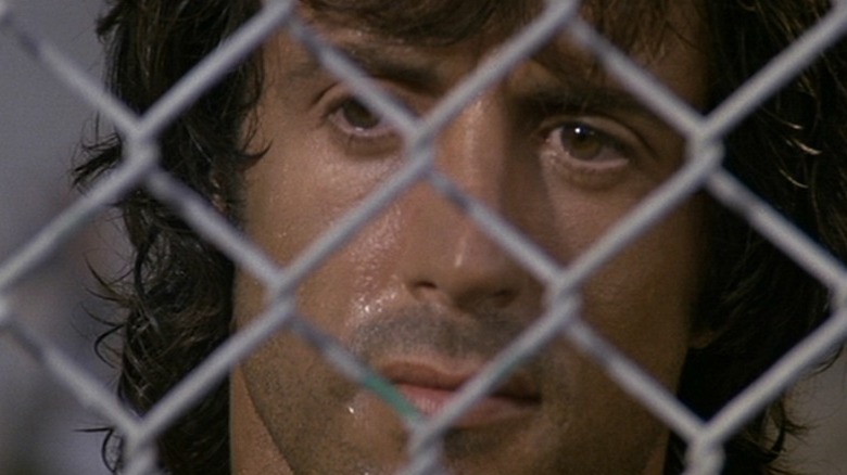 Sylvester Stallone's John Rambo stands behind a fence in Rambo: First Blood Part II