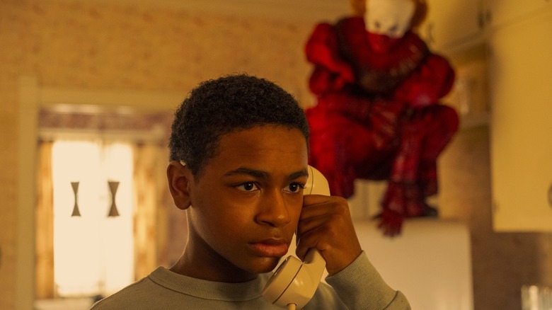 Blake Cameron James' Will Hanlon holds a phone to his ear as Bill Skarsgård's Pennywise crouches in the background in It Welcome to Derry