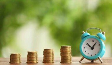 Four vertical stacks of coins growing in height from left to right next to an old style alarm clock