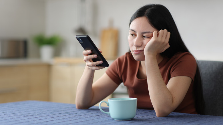 Girl sitting at a table with her smartphone, an annoyed look on her face