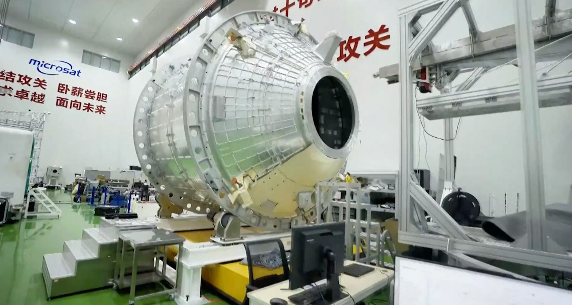 A large metal spacecraft is sits on a platform in a warehouse with lettering behind it