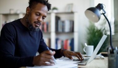 Young investor sitting at a desk, reviewing paperwork with open laptop close at hand.