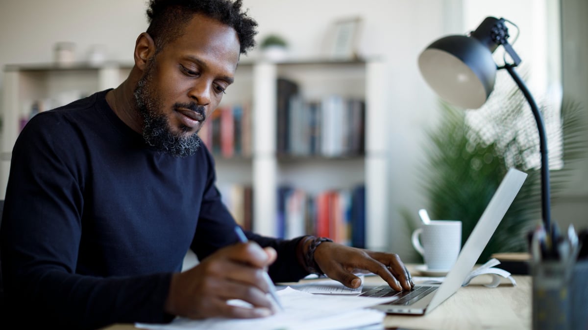 Young investor sitting at a desk, reviewing paperwork with open laptop close at hand.