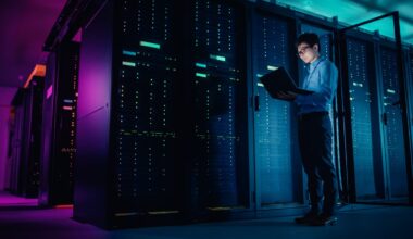 A man standing in front of a line of server racks with a laptop open.