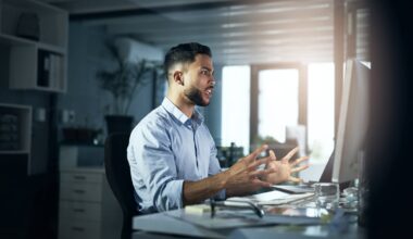 An angry person with hands outstretched looking at a computer monitor.