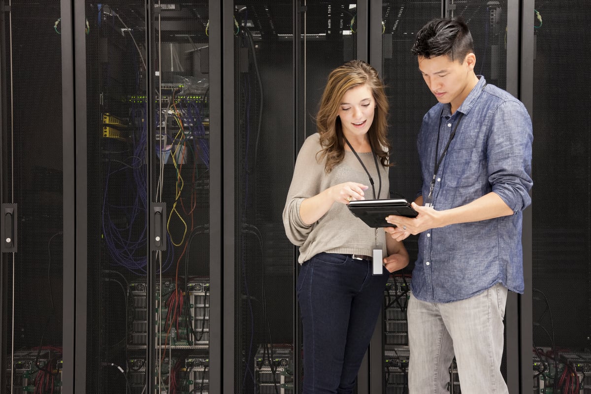 People viewing a mobile device in front of stacks of data center servers.