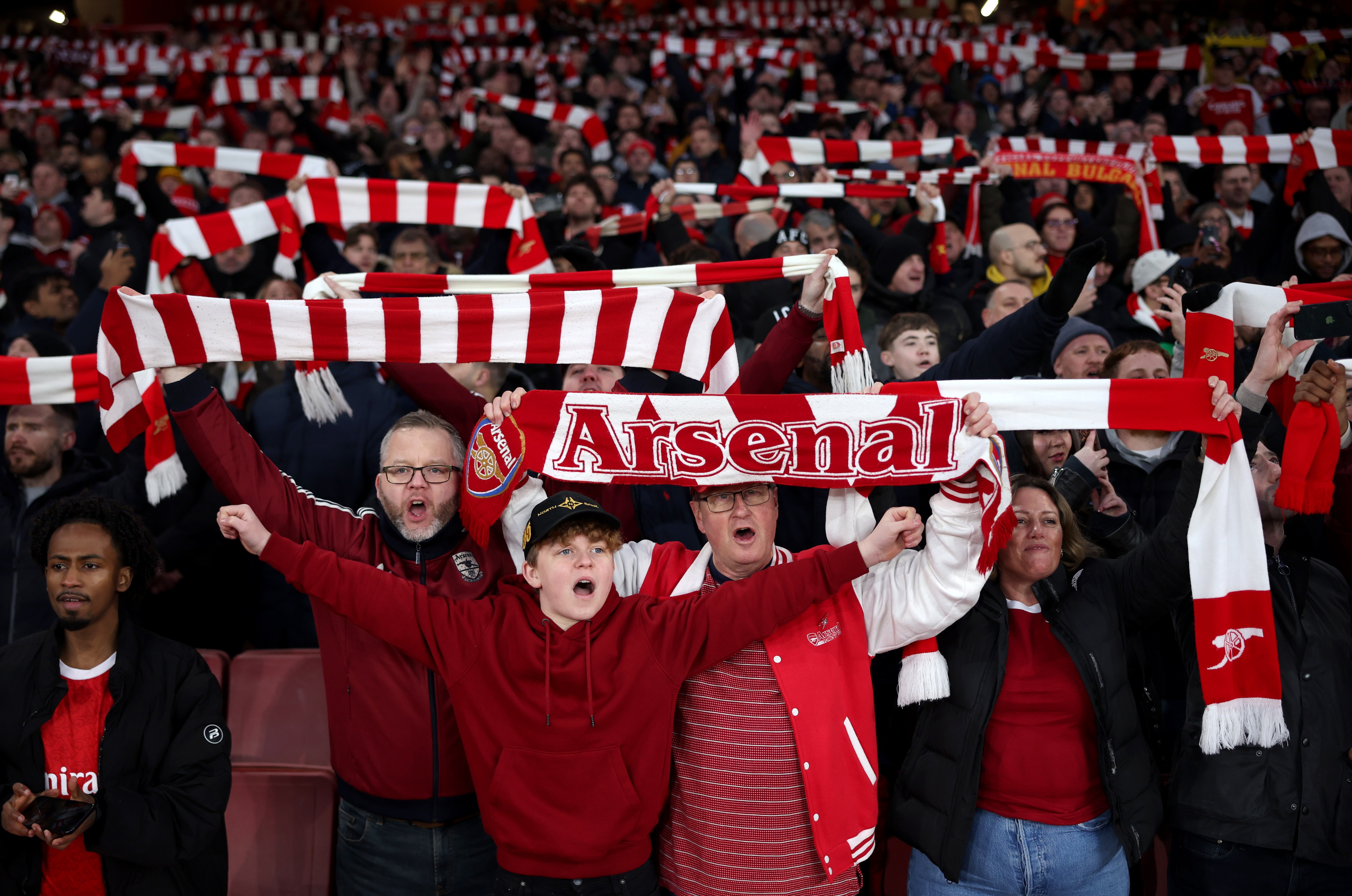 Fans of Arsenal Football Club hold scarves aloft in the stands.