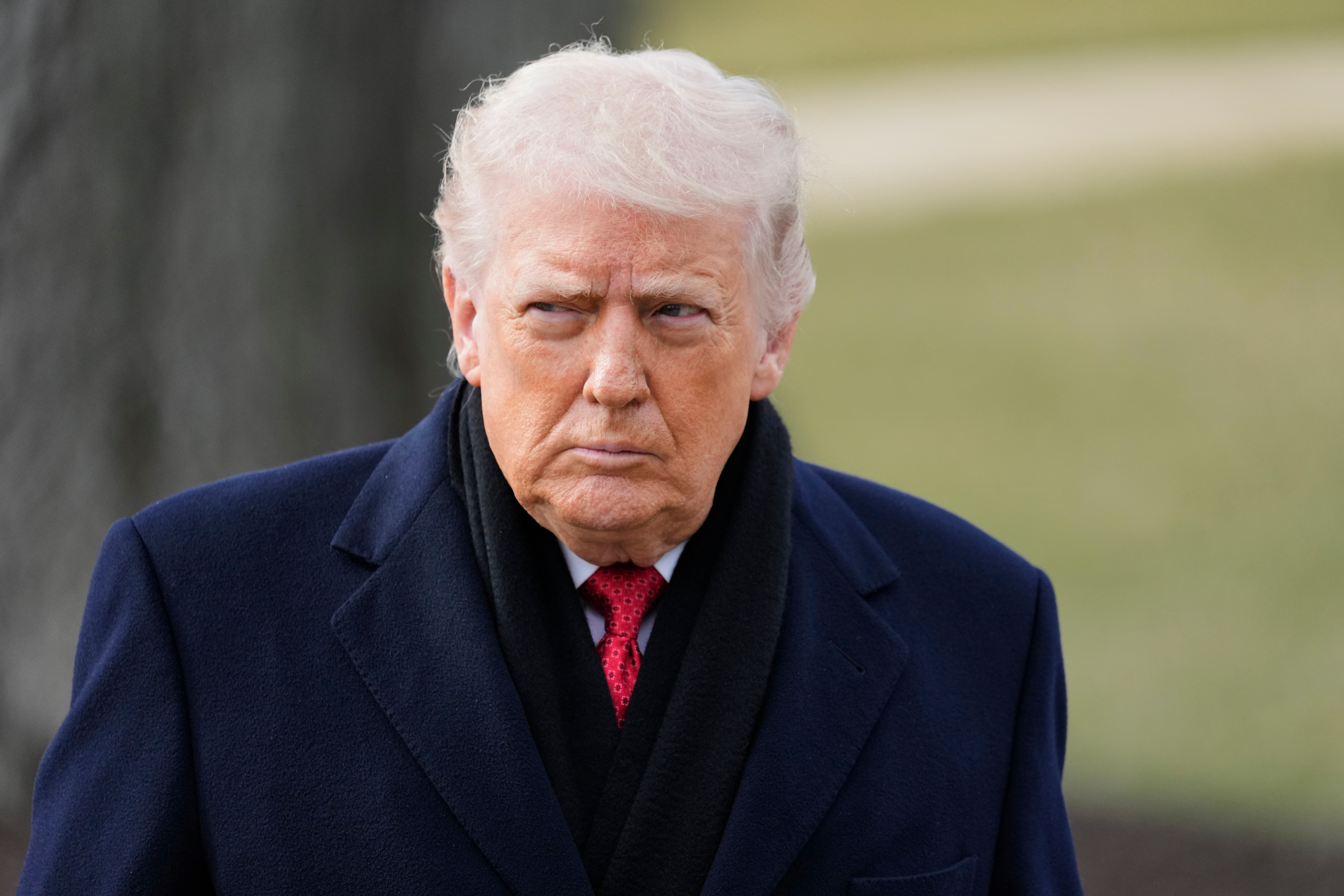 Donald Trump in a navy coat and red tie looking towards the left.