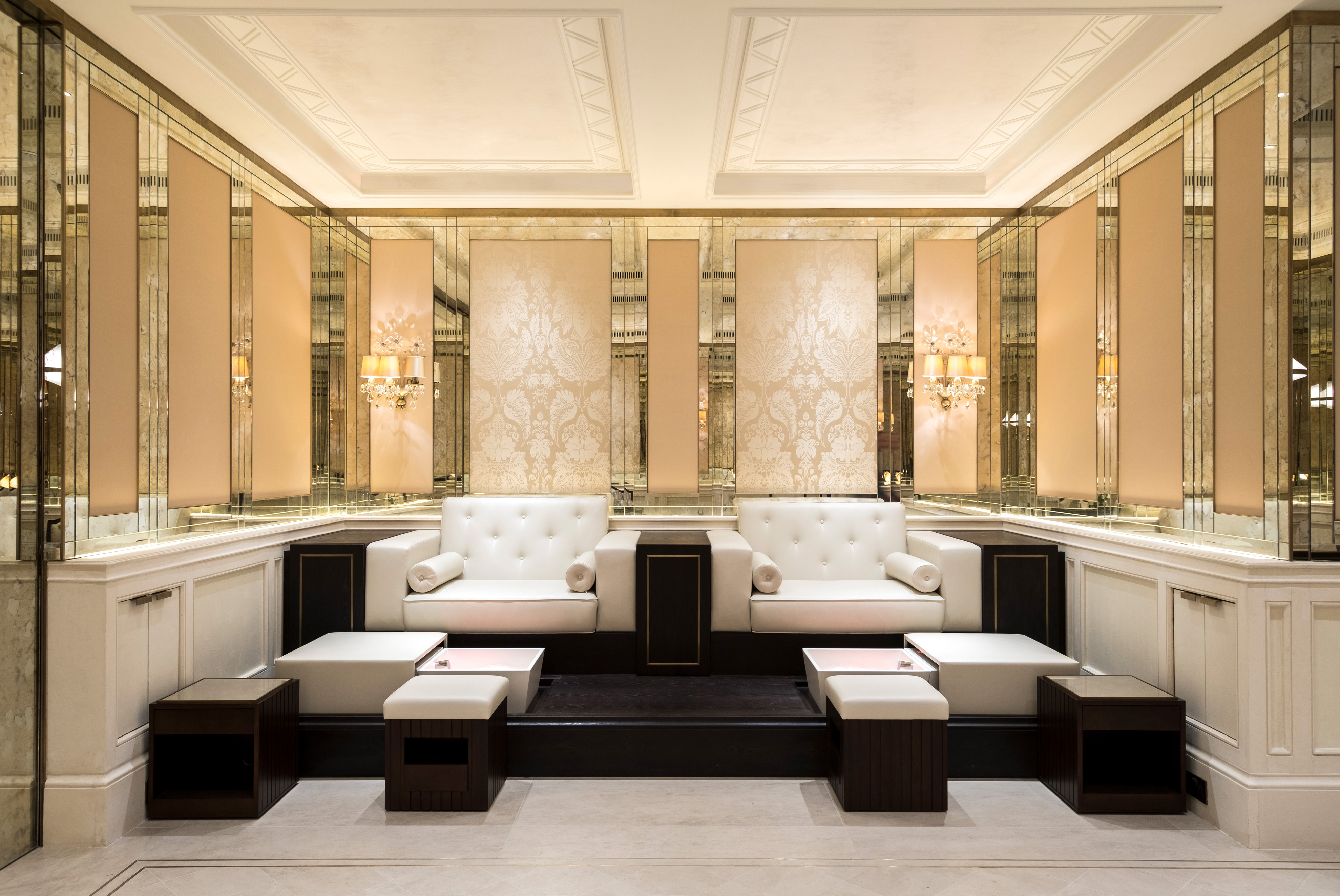 Lounge area at the Lanesborough Club and Spa with two cream sofas, small tables, and mirrored walls.