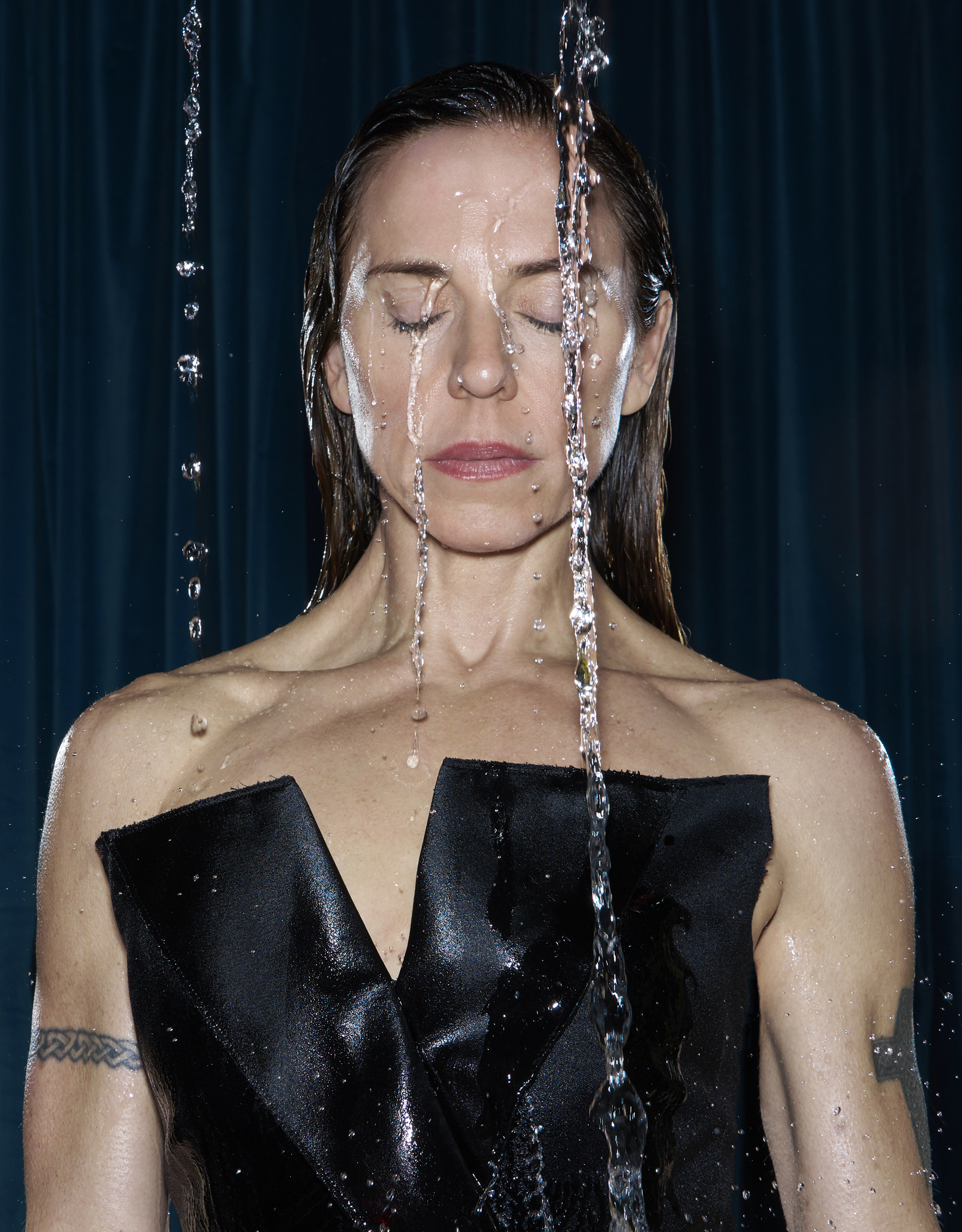 Melanie C, with closed eyes, with water splashing on her face and bare shoulders, wearing a black top.