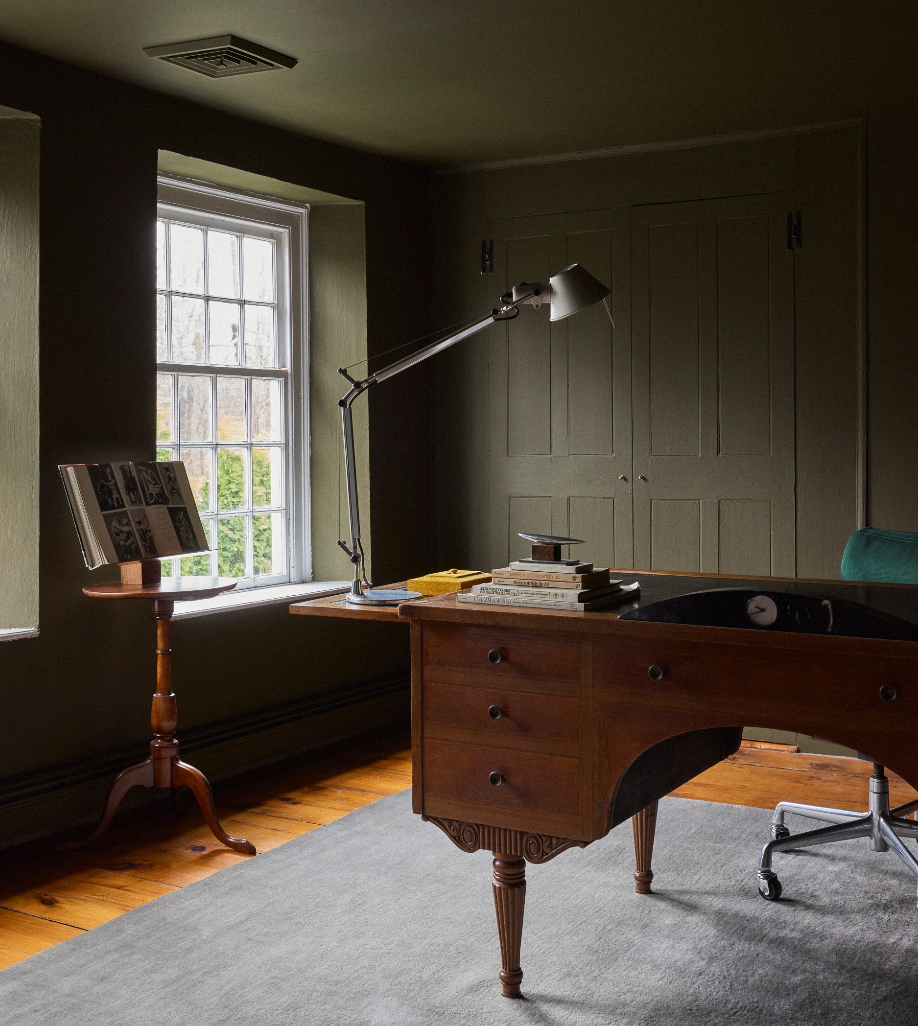A home office with olive green walls, a wooden desk, and a light gray rug.