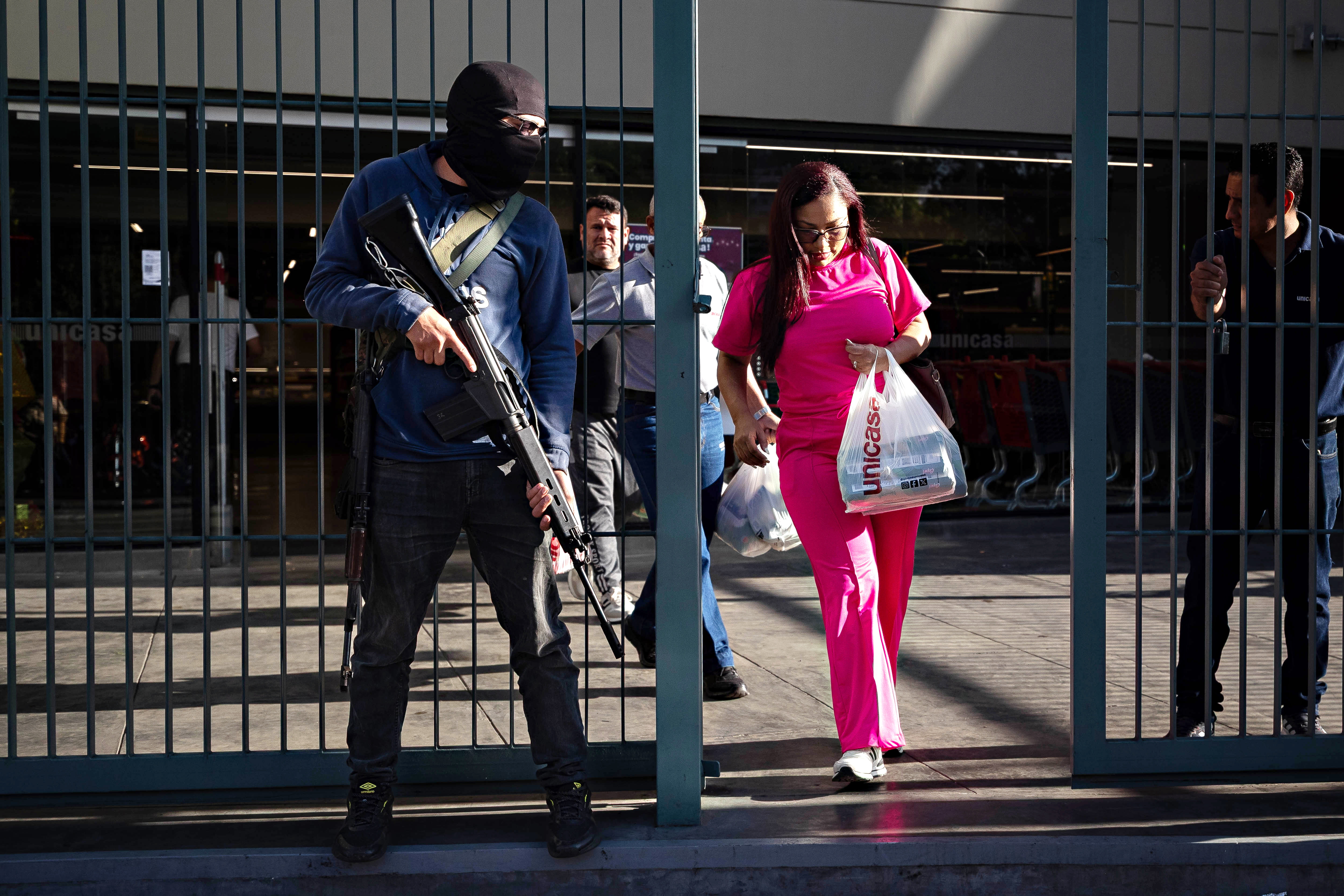 A masked man with a rifle guards the entrance to a supermarket.