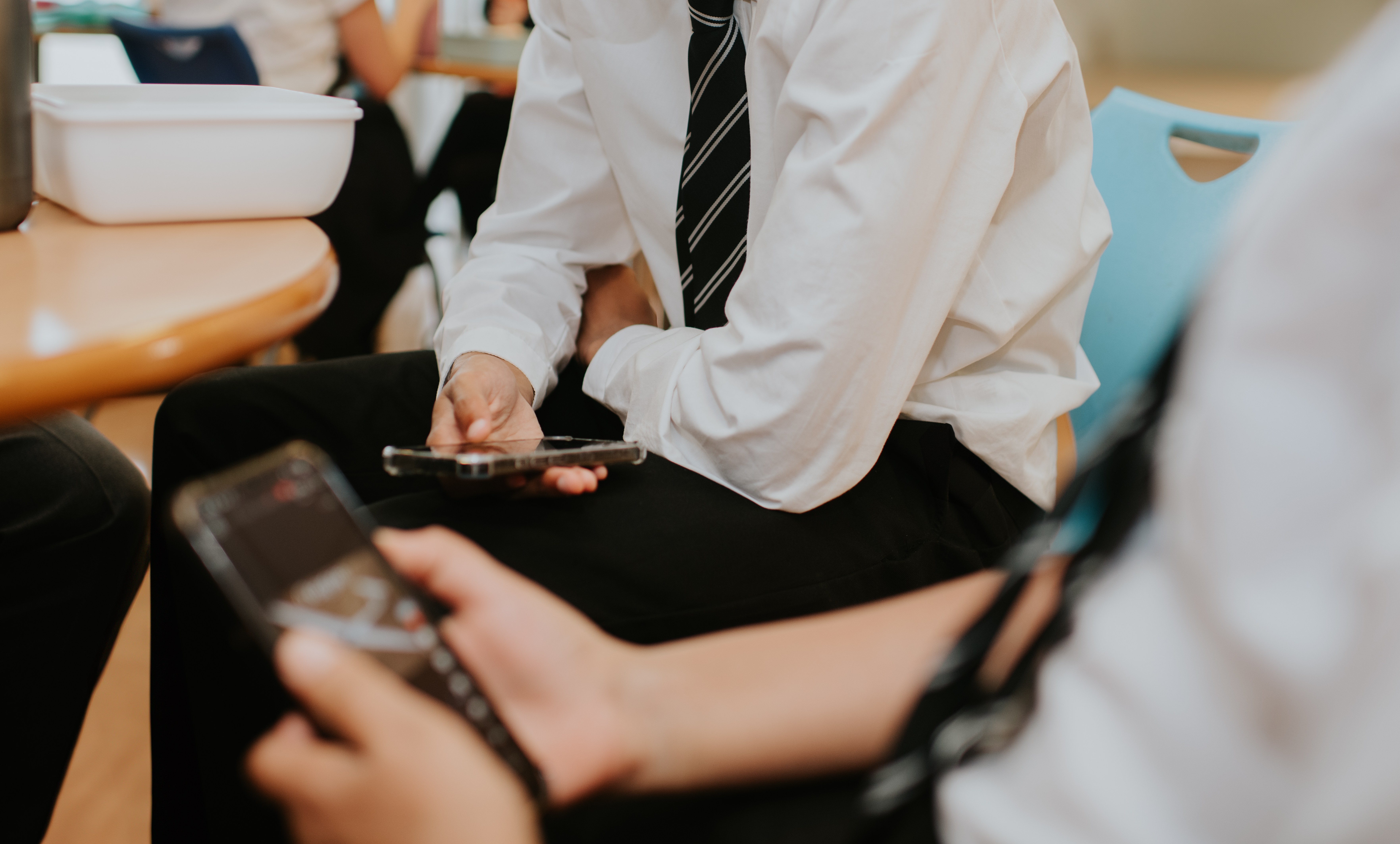 Two schoolboys are glued to their smartphones during lunch break in a cafeteria.