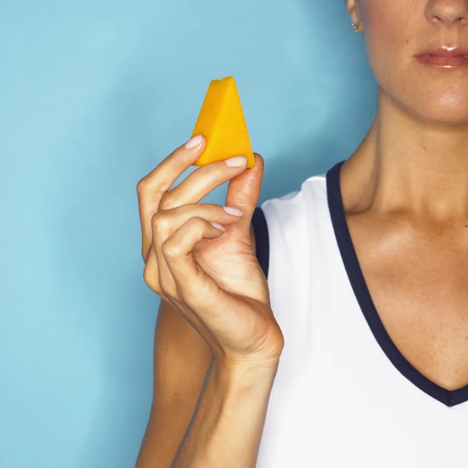 Person holding a triangular piece of cheese with a blue background