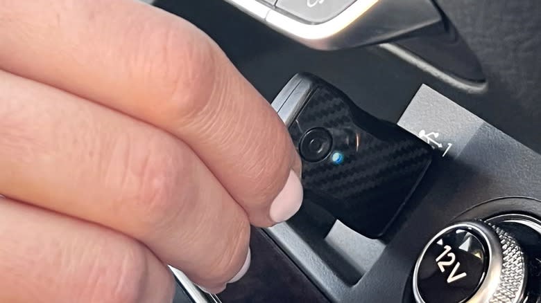 A person plugging an Aluratek wireless car adapter into their dashboard.