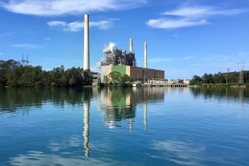 Vales Point Power Station sits to the right of image over lake on a clear blue day. Smoke comes out of building.