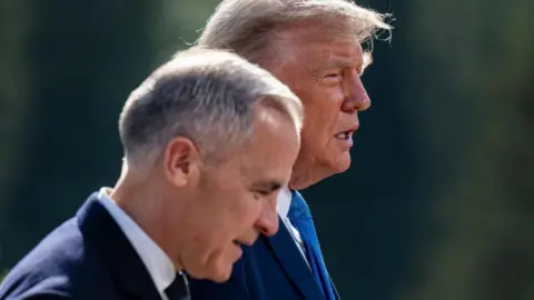 EPA Prime Minister Mark Carney, slightly out of focus, walks in profile next to President Donald Trump. 