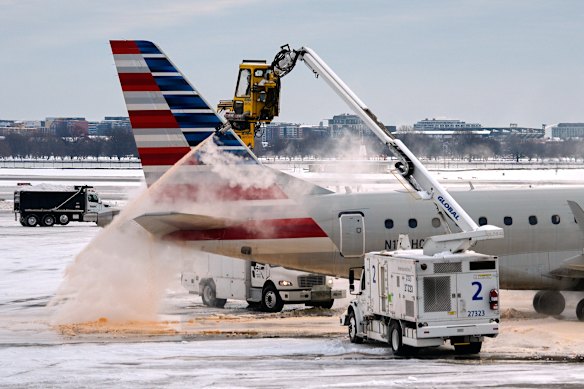 Ground crew work to clear snow and ice from an aircraft at Ronald Reagan National Airport in Washington. Thousands of flights have been delayed or cancelled due to the weather.